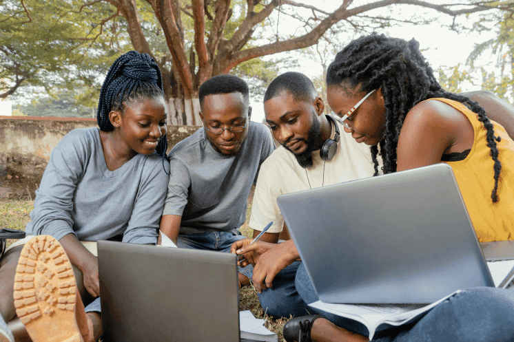 Four university students working together over laptops and notes outdoors on campus